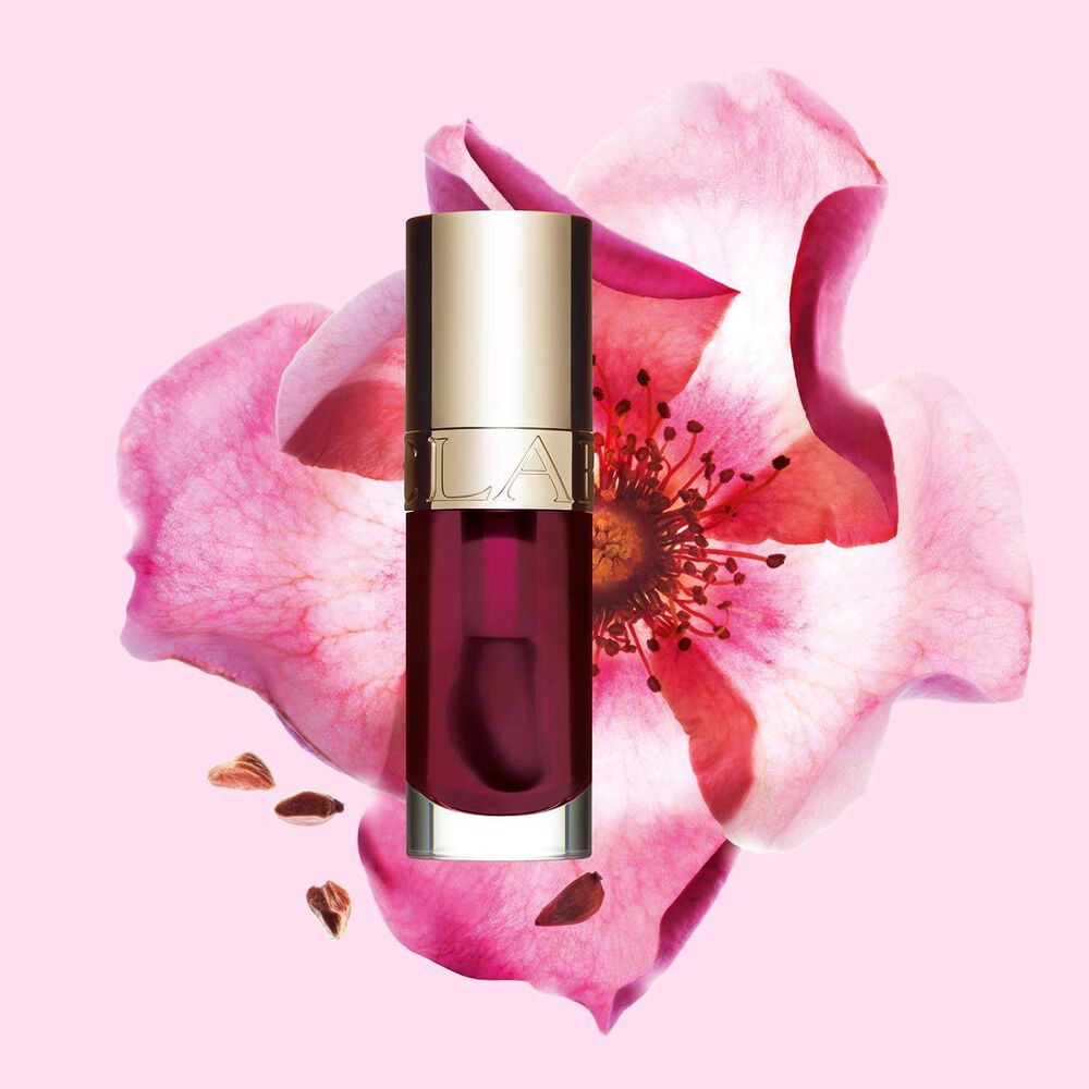 Packshot of Clarins Lip Comfort Oil Fig, placed next to a sweetbriar rose on a light pink background.