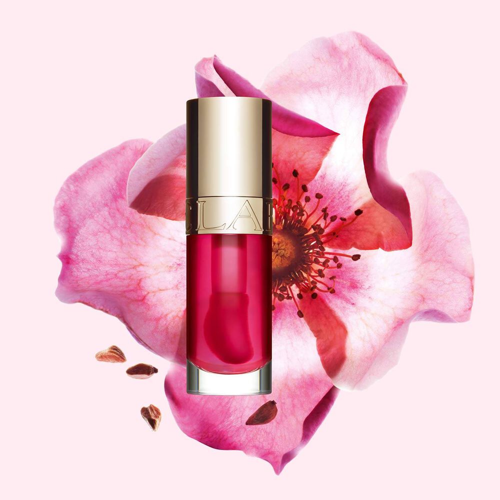 Packshot of Clarins Lip Comfort Oil in Pitaya, placed next to a sweetbriar rose on a light pink background.