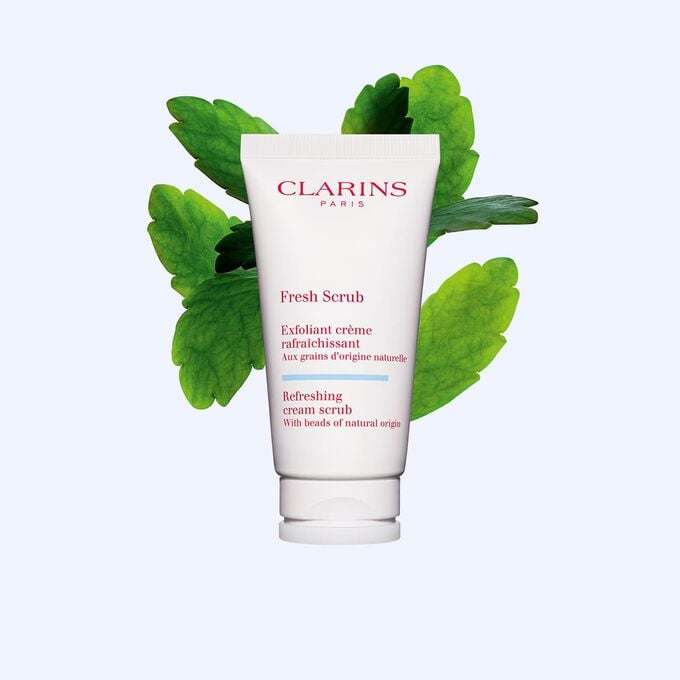 Packshot of Clarins face exfoliant Fresh Scrub tube next to some leaves of life on a white background.