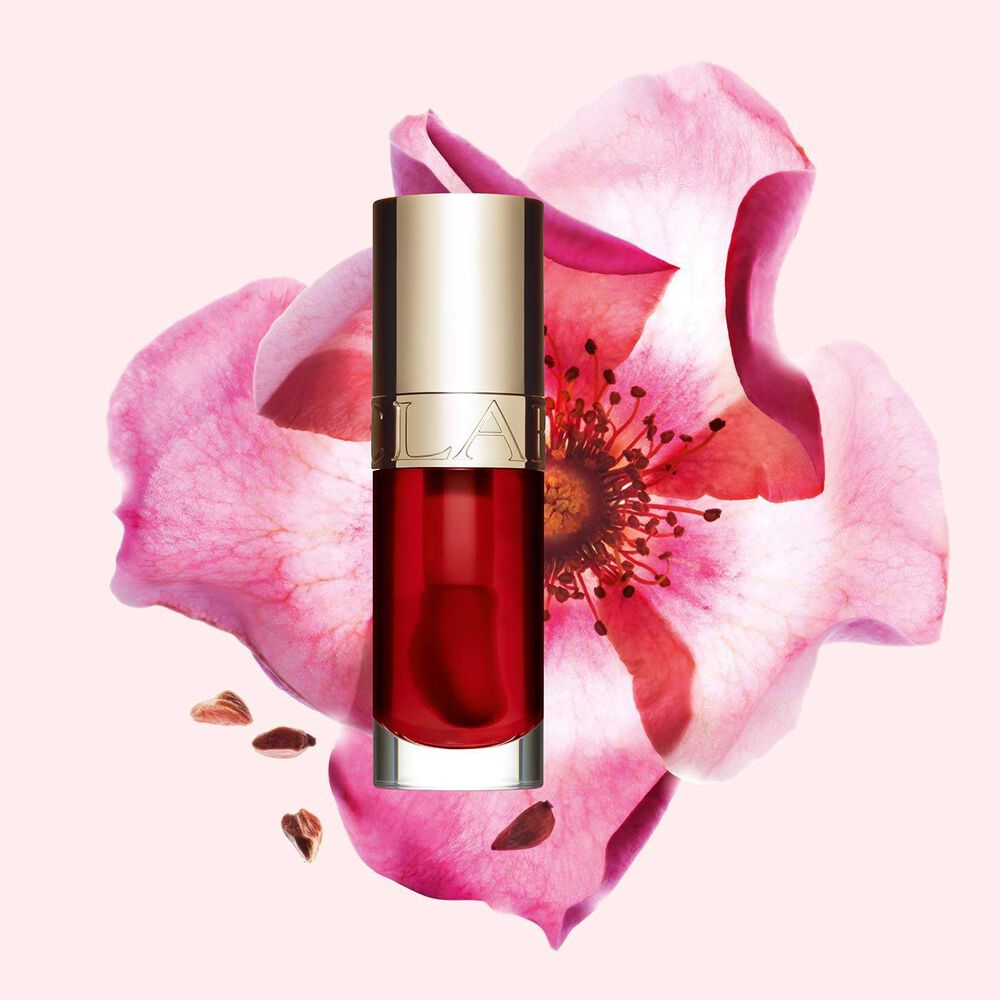 Packshot of Clarins Lip Comfort Oil Strawberry, placed next to a sweetbriar rose on a light pink background.