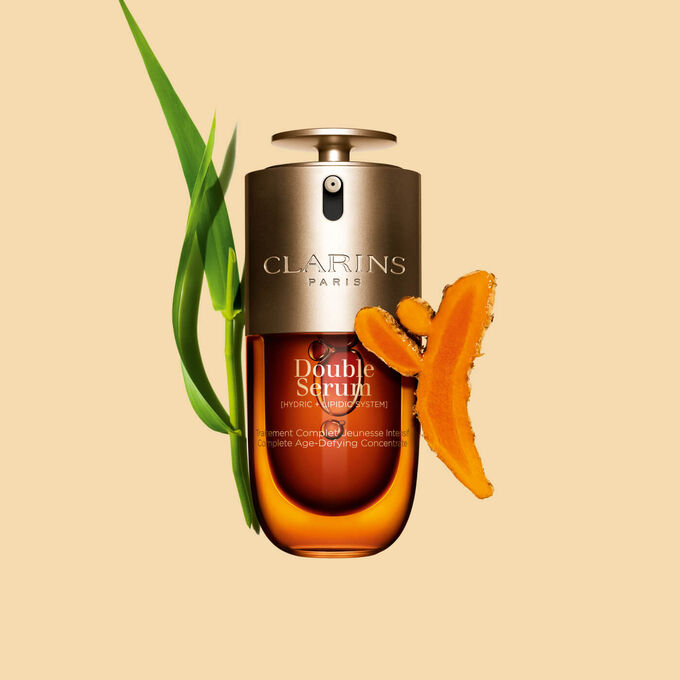Packshot of the Clarins Double Serum displayed in front of its ingredient, including curcuma, on a gold background