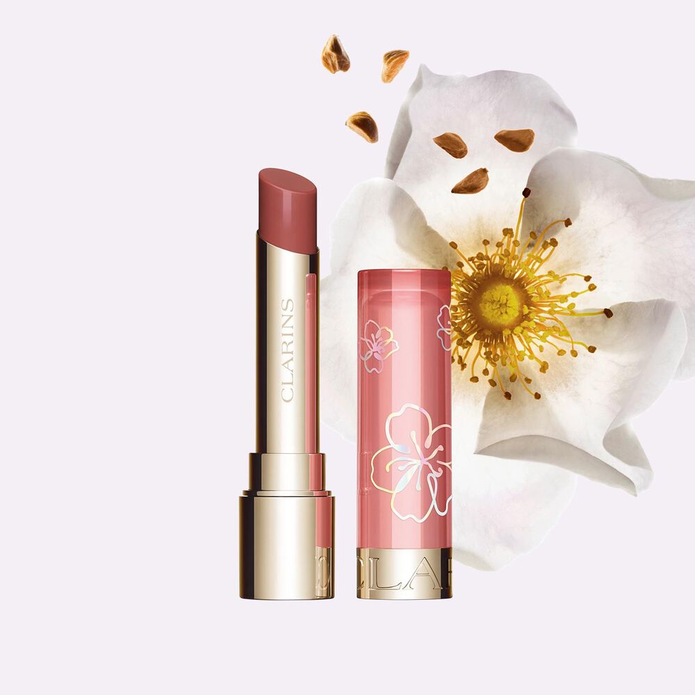 Packshot of a tube of Clarins Fairy Blossoms Lip Oil Balm in a pink shade with a flower on the side over a pink background.