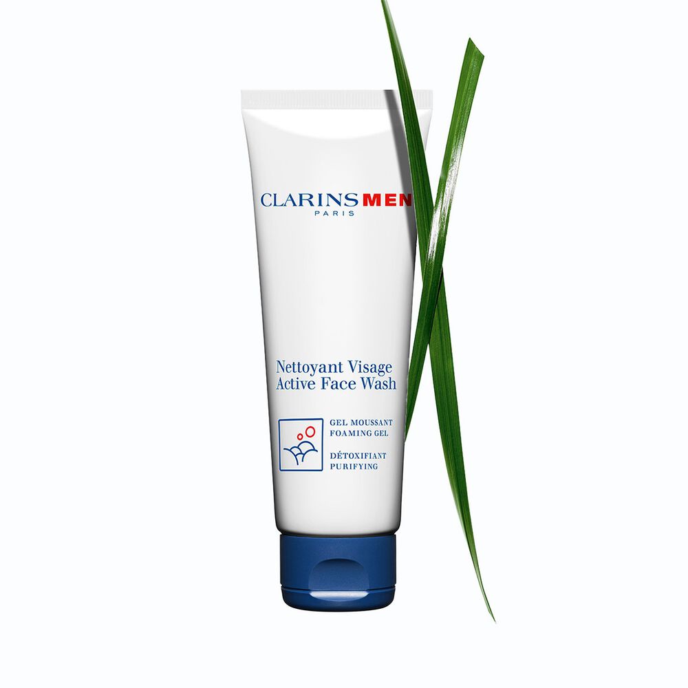 Packshot of the Active Face Wash, men's face cleanser by Clarins next to bison grass to emphasize its key ingredient.