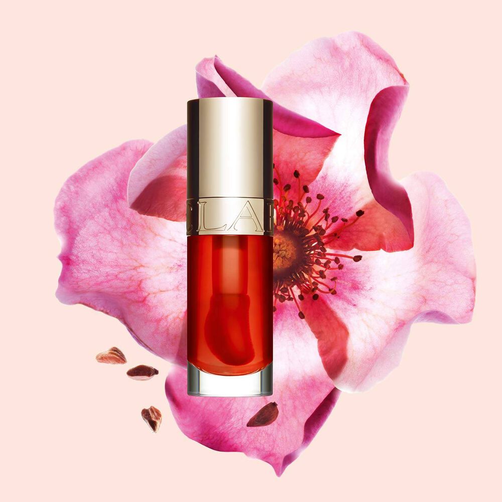 Packshot of Clarins Lip Comfort Oil Apricot, placed next to a sweetbriar rose on a light orange peach background.