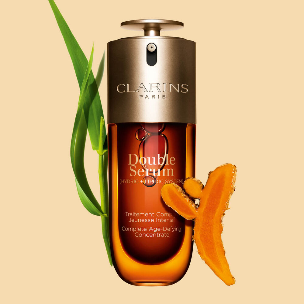 Packshot of the Clarins Double Serum displayed in front of its ingredient, including curcuma, on a gold background