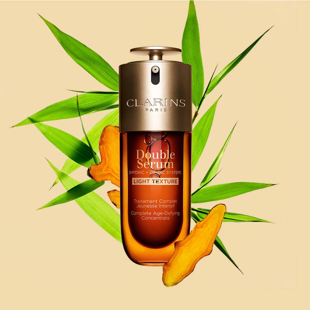 A 50ml bottle of Clarins Double Serum Light Texture among turmeric and provençal reed leaves against an orange background.