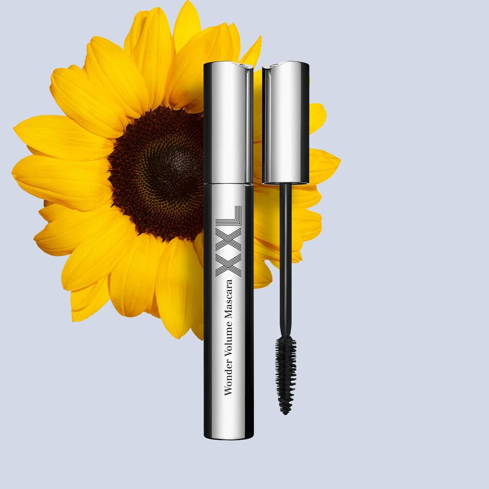 Packshot of an open lengthening black mascara by Clarins, displayed in front of a sunflower on a white background