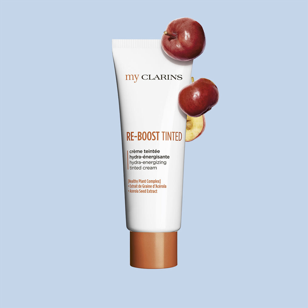 Packshot of a boosting and moisturizing tinted cream alongside acerola seeds on a light blue background.