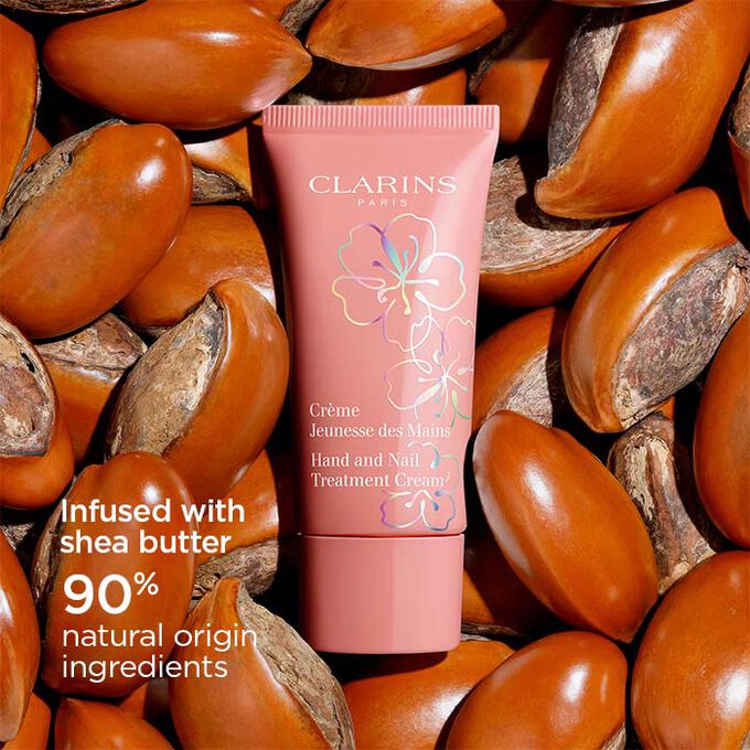 Packshot of Clarins Fairy Blossoms Hand Cream surrounded by shea butter seeds, highlighting its 90% natural origin formula.